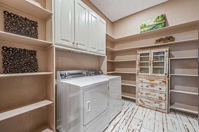 clothes washing area featuring cabinets, washing machine and clothes dryer, and light hardwood / wood-style floors