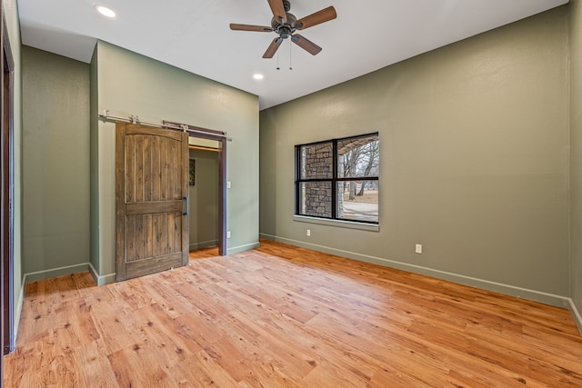 empty room with ceiling fan, light hardwood / wood-style flooring, and a barn door