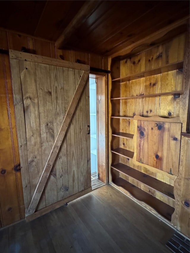 interior space featuring a barn door, dark wood-type flooring, wooden ceiling, and wood walls