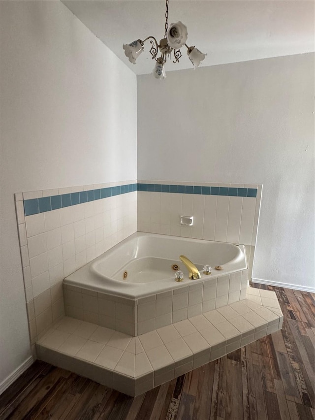 bathroom with hardwood / wood-style floors, a chandelier, and tiled tub