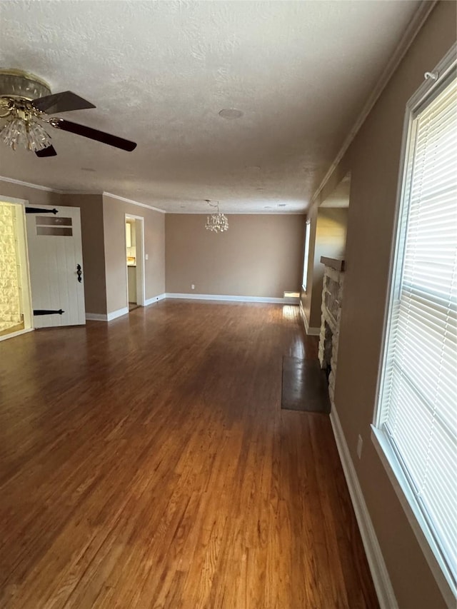 unfurnished living room featuring crown molding, ceiling fan with notable chandelier, dark wood-type flooring, and a textured ceiling