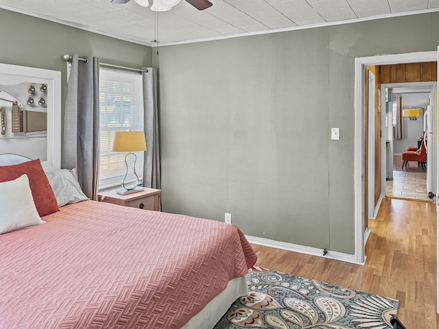 bedroom featuring a ceiling fan, baseboards, ornamental molding, and wood finished floors