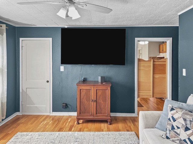 living room with light wood-style floors, baseboards, a ceiling fan, and ornamental molding