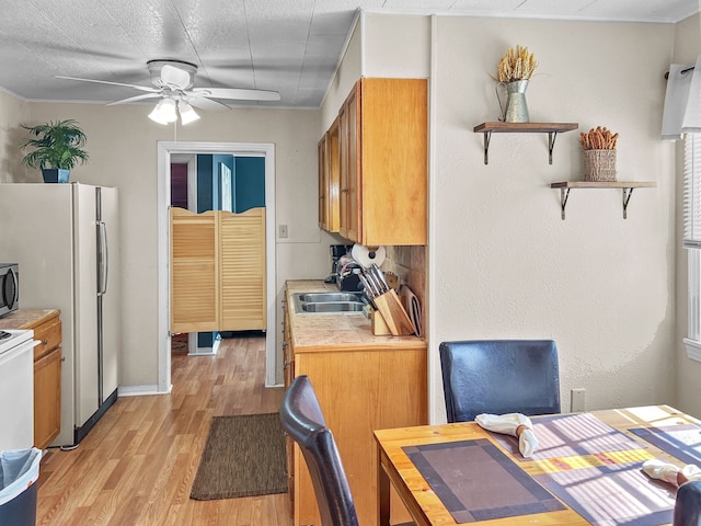 kitchen featuring light wood finished floors, stainless steel microwave, brown cabinets, light countertops, and a sink