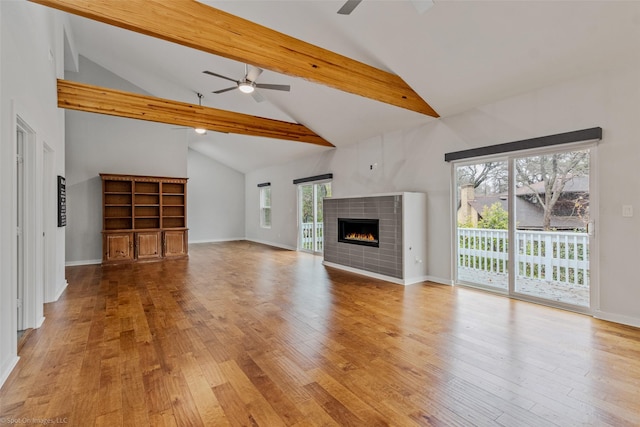 unfurnished living room featuring ceiling fan, beam ceiling, high vaulted ceiling, a fireplace, and light hardwood / wood-style floors