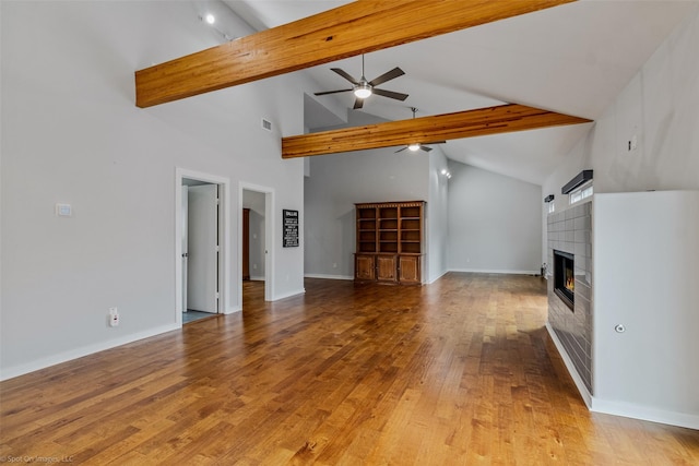 unfurnished living room with high vaulted ceiling, hardwood / wood-style flooring, ceiling fan, beam ceiling, and a tiled fireplace