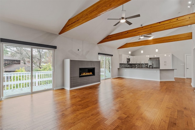 unfurnished living room featuring beam ceiling, high vaulted ceiling, ceiling fan, and light wood-type flooring