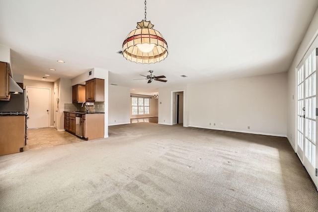 unfurnished living room with sink, light colored carpet, and ceiling fan