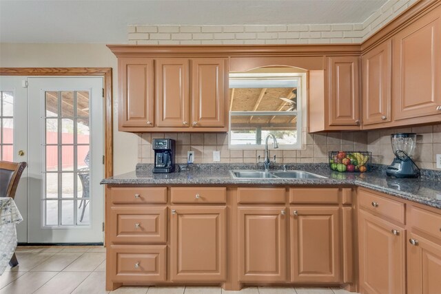 kitchen with light tile patterned floors, dark stone counters, sink, and backsplash