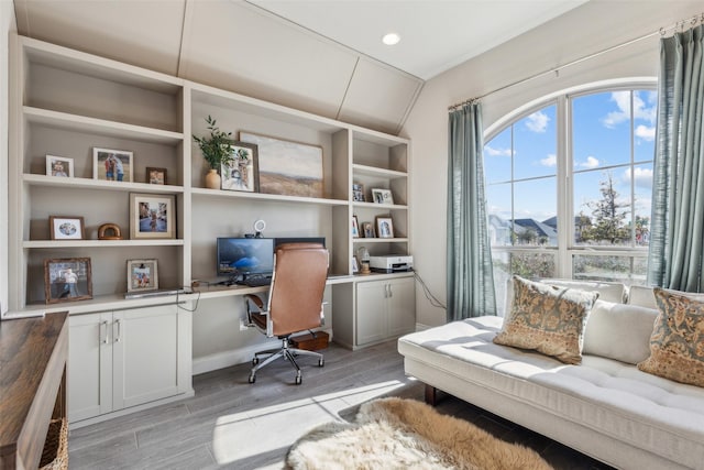 office space with vaulted ceiling, built in desk, and light wood-type flooring