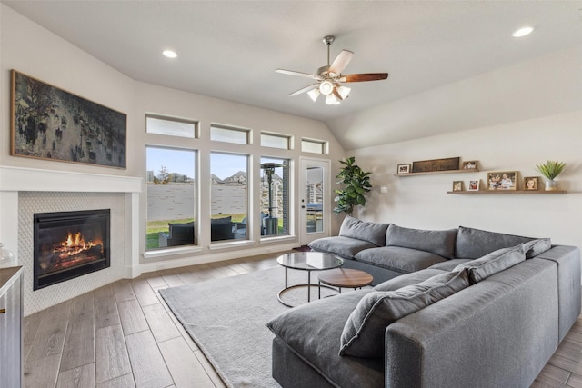 living room with a tiled fireplace, ceiling fan, vaulted ceiling, and light wood-type flooring