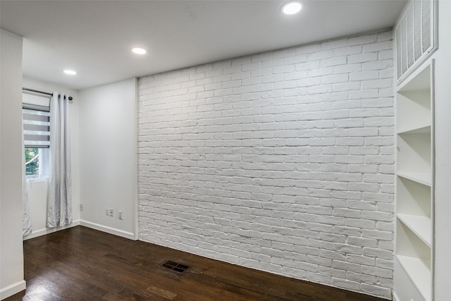 spare room with dark hardwood / wood-style flooring and brick wall