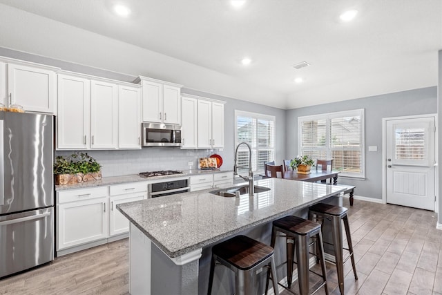 kitchen featuring sink, white cabinetry, light stone counters, a center island with sink, and stainless steel appliances