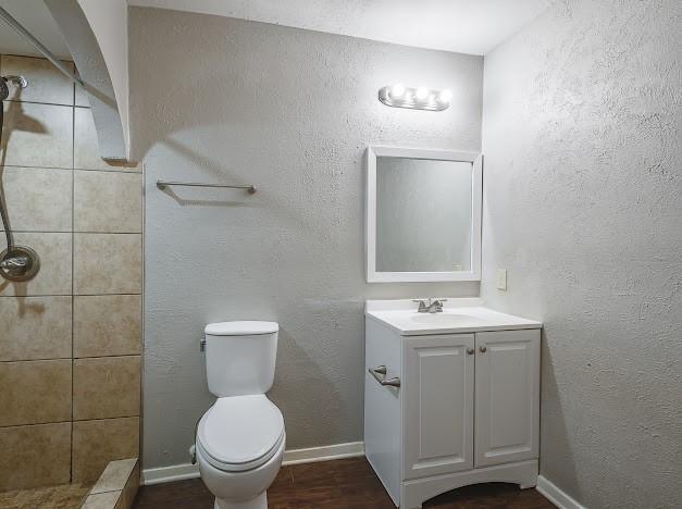 bathroom with vanity, hardwood / wood-style flooring, toilet, and a tile shower