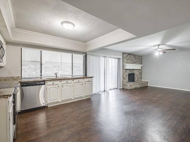 kitchen featuring appliances with stainless steel finishes, a fireplace, white cabinetry, dark hardwood / wood-style flooring, and crown molding