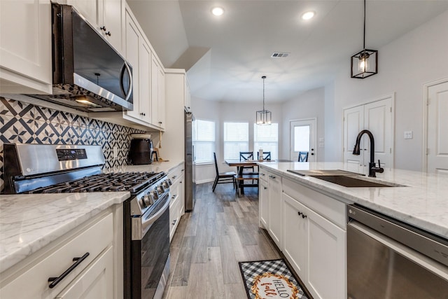 kitchen featuring white cabinetry, sink, decorative light fixtures, and appliances with stainless steel finishes