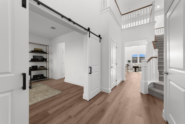 hall featuring a barn door, a towering ceiling, and light hardwood / wood-style flooring