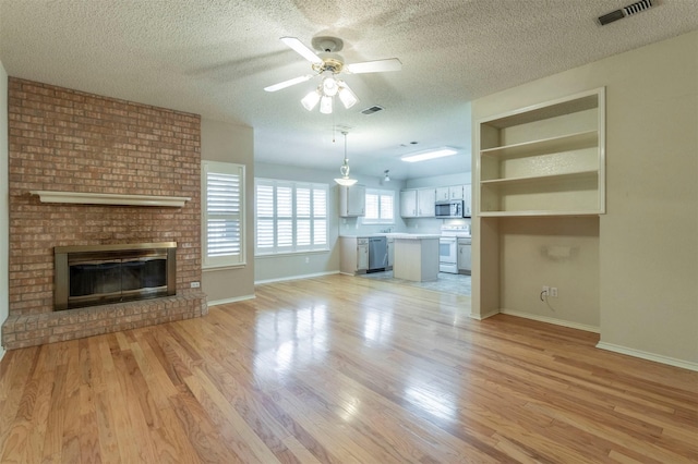 unfurnished living room with ceiling fan, light hardwood / wood-style floors, a brick fireplace, and a textured ceiling