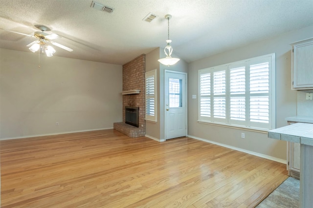 unfurnished living room with ceiling fan, a fireplace, light hardwood / wood-style flooring, and a textured ceiling