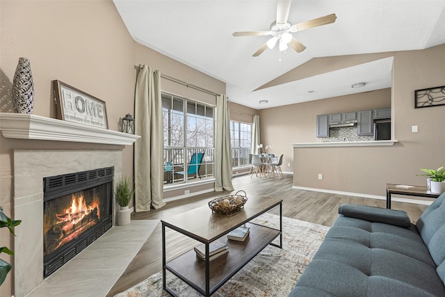 living area featuring lofted ceiling, a ceiling fan, a high end fireplace, baseboards, and light wood finished floors