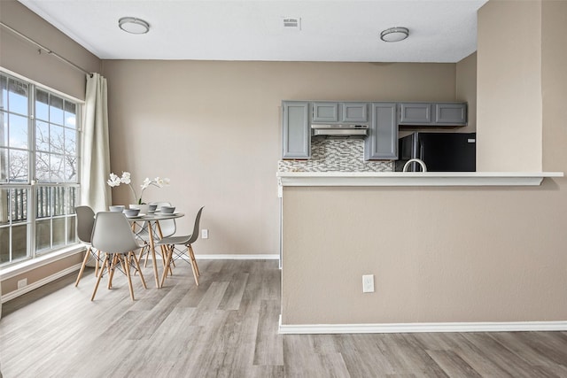 kitchen with black fridge, light wood-type flooring, decorative backsplash, and gray cabinetry