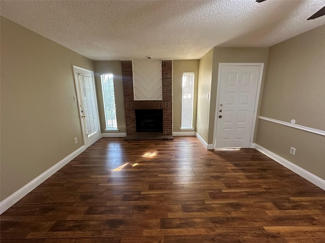 unfurnished living room with ceiling fan, a brick fireplace, dark wood-type flooring, and a textured ceiling