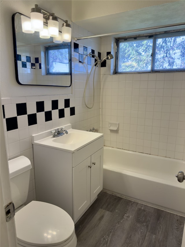 full bathroom featuring tiled shower / bath, tile walls, hardwood / wood-style flooring, vanity, and toilet