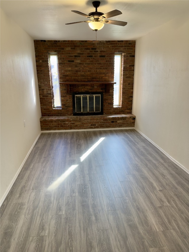 unfurnished living room with hardwood / wood-style flooring, a fireplace, ceiling fan, and brick wall