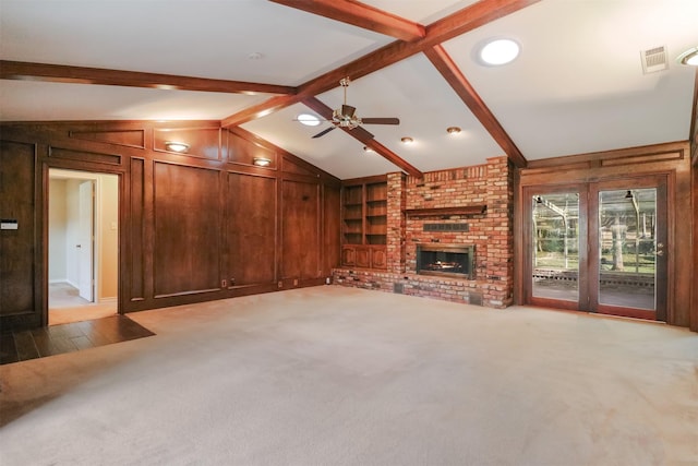 unfurnished living room with built in features, vaulted ceiling with beams, a fireplace, light colored carpet, and wood walls