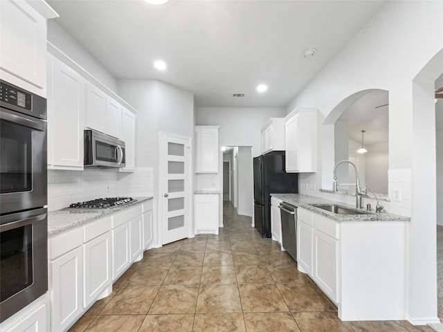 kitchen with stainless steel appliances, light stone countertops, backsplash, sink, and white cabinetry