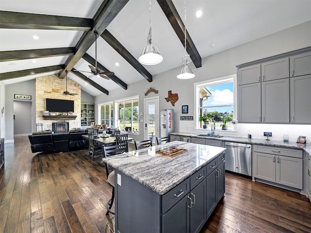 kitchen with a stone fireplace, gray cabinetry, light stone counters, stainless steel dishwasher, and a kitchen island