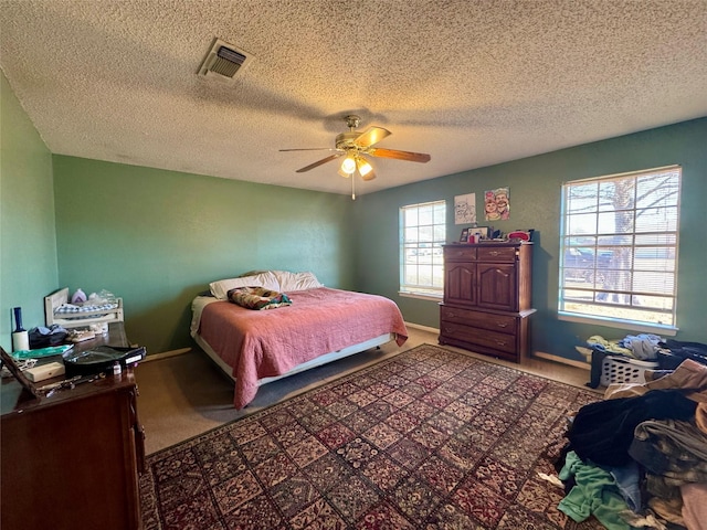 bedroom featuring a ceiling fan, a textured ceiling, visible vents, and carpet