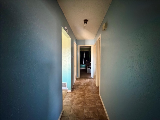 hall with baseboards, a textured wall, and tile patterned flooring