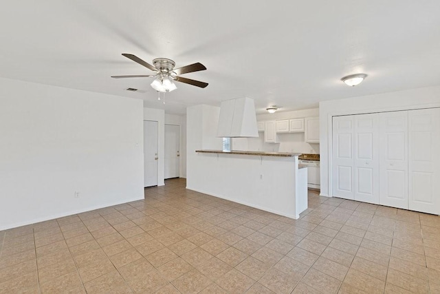 kitchen with ceiling fan, a peninsula, visible vents, white cabinetry, and baseboards