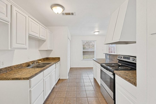 kitchen featuring dishwasher, dark countertops, stainless steel range with electric stovetop, white cabinetry, and a sink