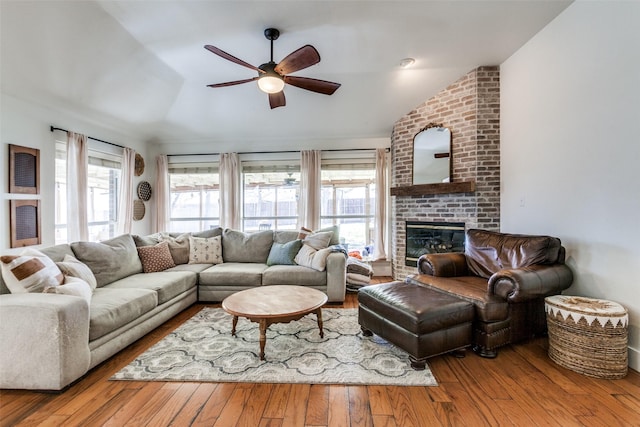 living room featuring ceiling fan, a brick fireplace, vaulted ceiling, and light hardwood / wood-style flooring