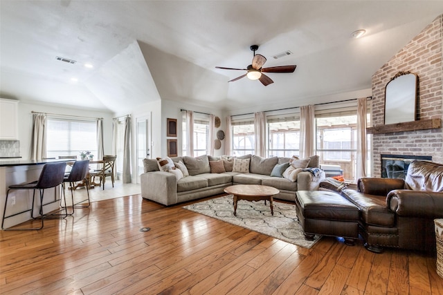 living room with vaulted ceiling, a brick fireplace, ceiling fan, and light wood-type flooring