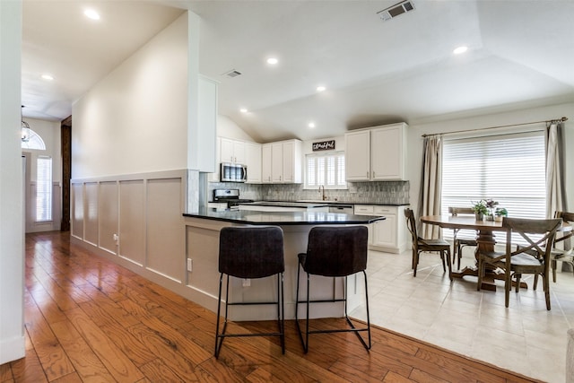 kitchen featuring a breakfast bar area, light wood-type flooring, appliances with stainless steel finishes, kitchen peninsula, and white cabinets