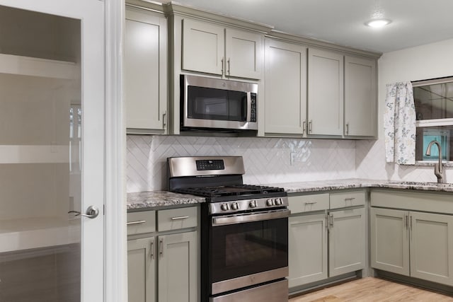 kitchen with stainless steel appliances, light stone countertops, sink, and backsplash