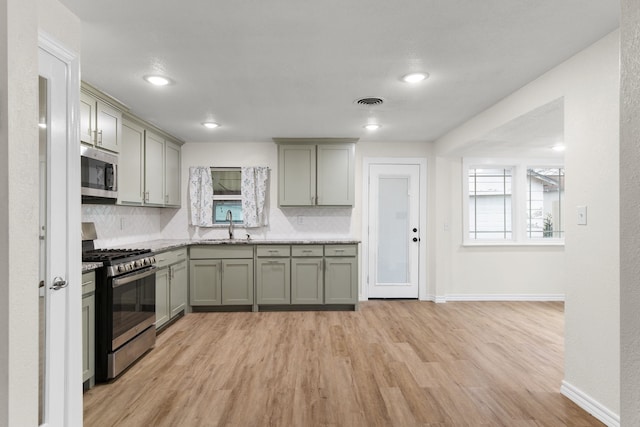 kitchen featuring gray cabinets, sink, backsplash, stainless steel appliances, and light wood-type flooring