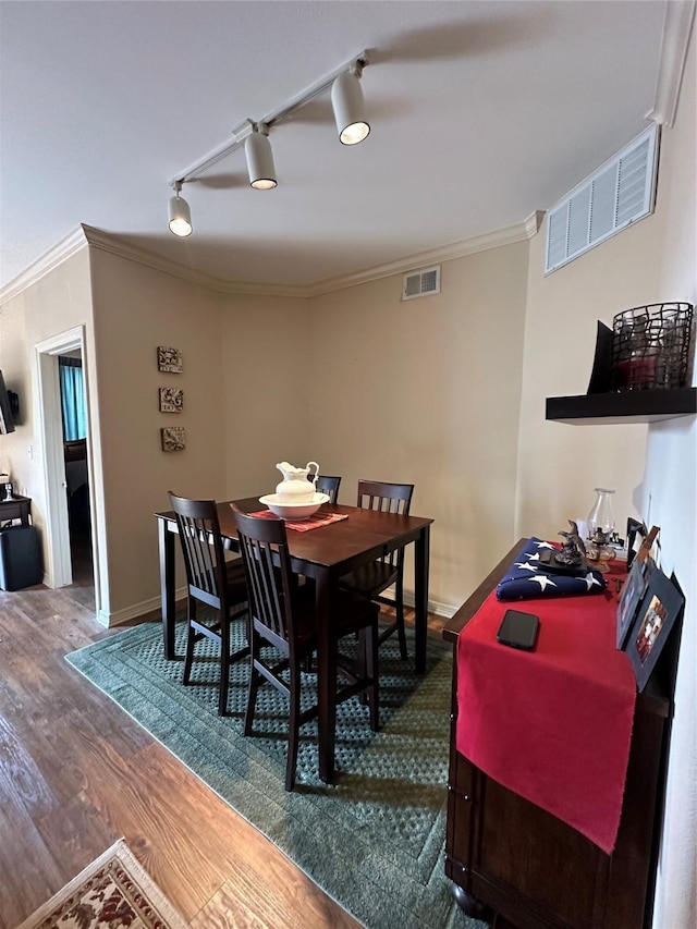 dining space with dark hardwood / wood-style flooring, track lighting, and ornamental molding