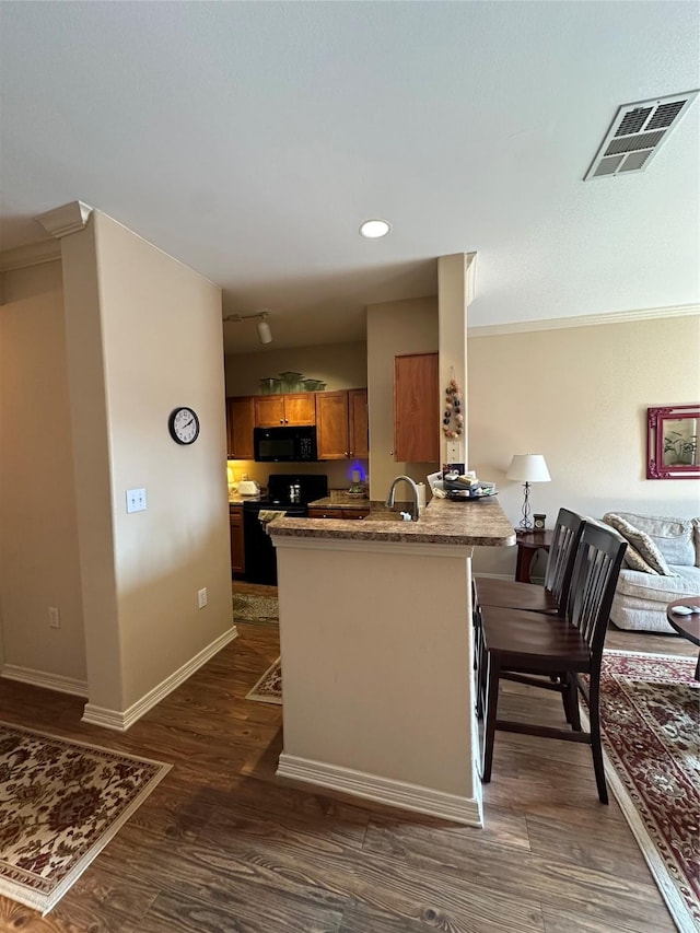 kitchen with black appliances, sink, a kitchen bar, kitchen peninsula, and dark wood-type flooring