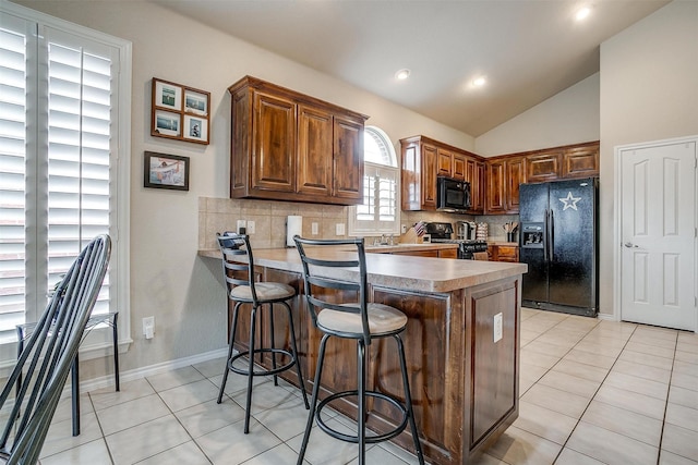 kitchen with a breakfast bar, black appliances, backsplash, light tile patterned floors, and kitchen peninsula