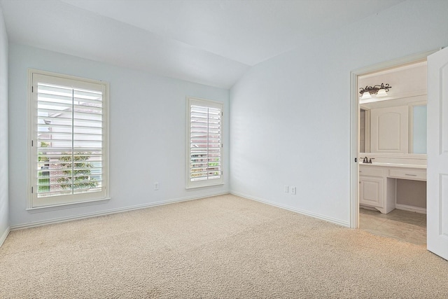 unfurnished bedroom featuring baseboards, light carpet, ensuite bath, and vaulted ceiling