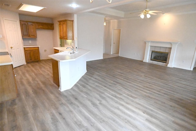 kitchen with sink, ceiling fan, a tiled fireplace, kitchen peninsula, and light wood-type flooring