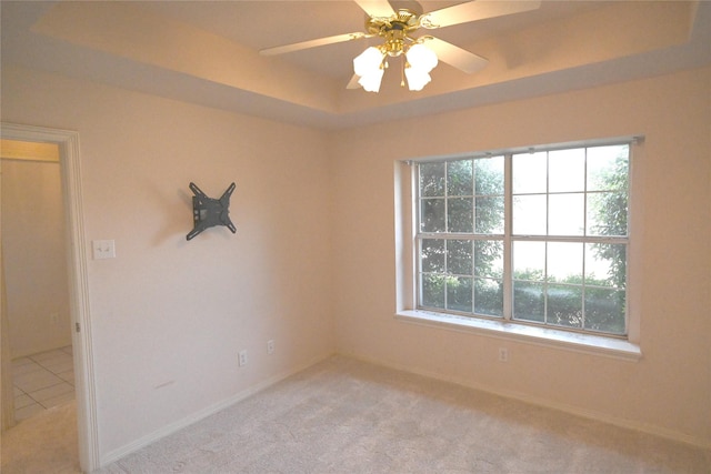 empty room with a raised ceiling, a healthy amount of sunlight, and light carpet