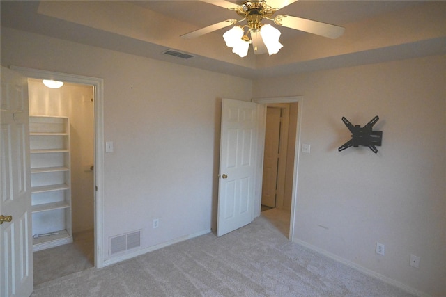 unfurnished bedroom with ceiling fan, a raised ceiling, and light carpet