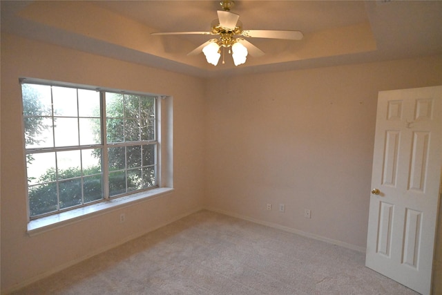 spare room with ceiling fan, light colored carpet, plenty of natural light, and a raised ceiling