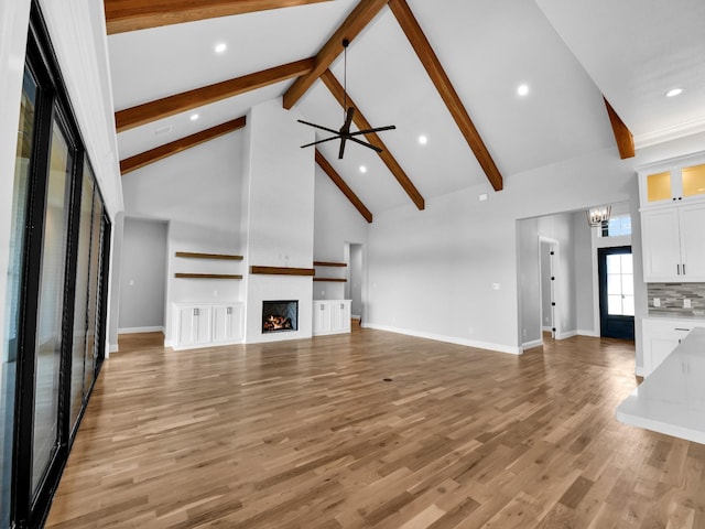 unfurnished living room featuring ceiling fan with notable chandelier, high vaulted ceiling, beamed ceiling, a large fireplace, and hardwood / wood-style flooring