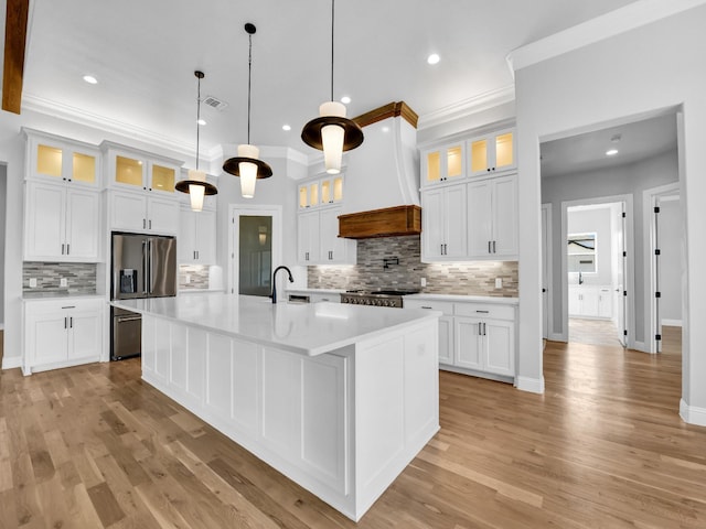 kitchen featuring premium range hood, stainless steel fridge, pendant lighting, a kitchen island with sink, and white cabinets